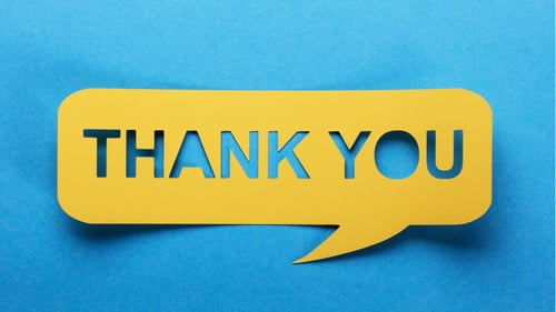 A yellow paper cut out of a talk bubble that says, Thank You, on a blue background.