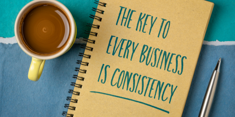 A notebook with, "The Key to Every Business is Consistency" written on it, sitting next to a cup of coffee.
