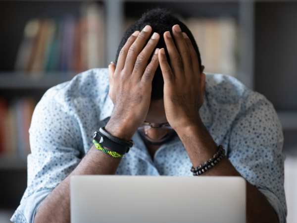 A person sitting in front of a laptop with their head in their hands.