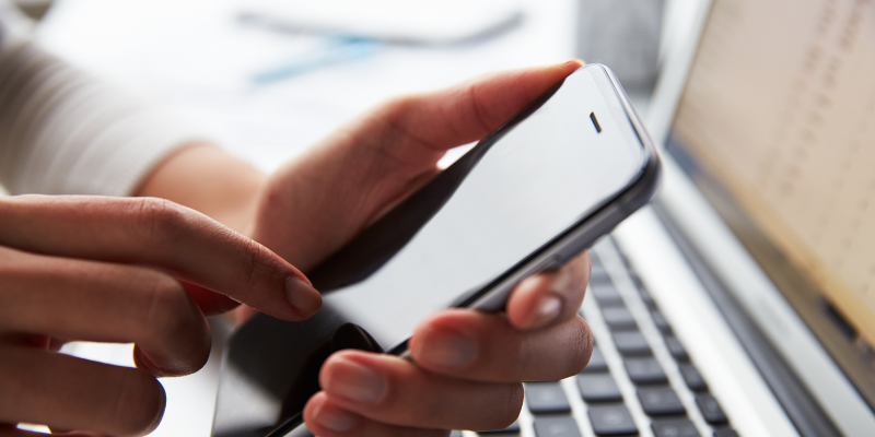 A person clicking their cellphone while working at their laptop.