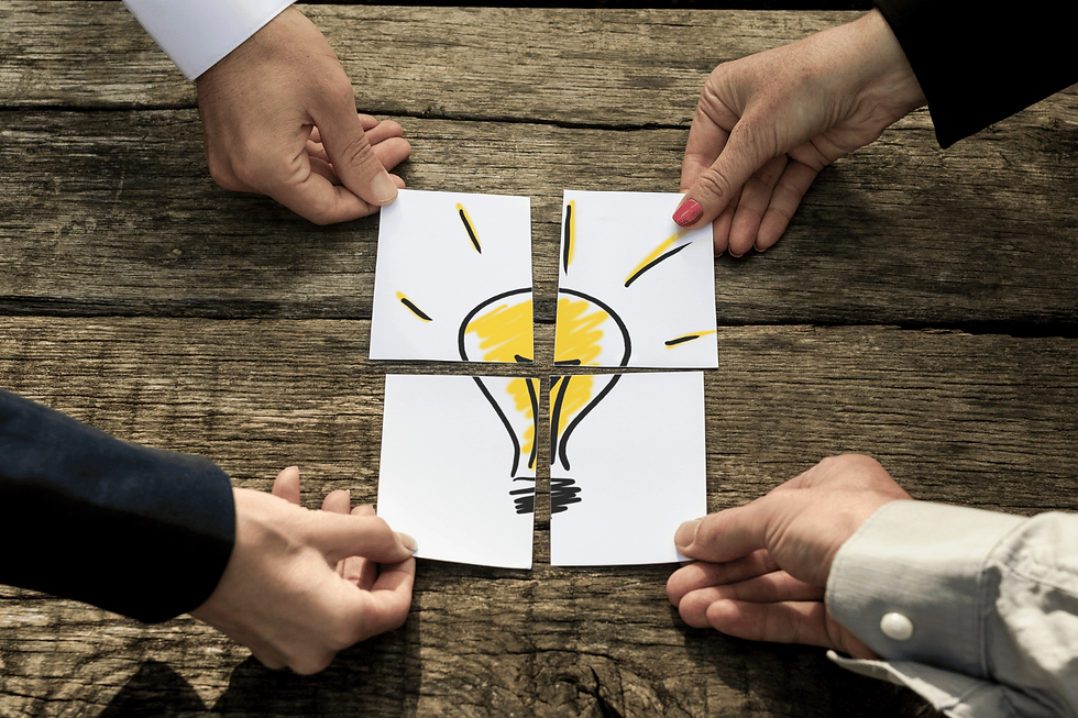 Four business owners putting pieces of paper together that make a drawing of a bright lightbulb.