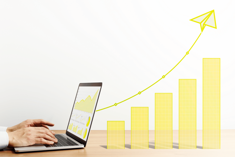 A person working on their laptop tracking marketing results and ROI. Next to the laptop is a graphic of a bar chart and a steady increase going up.