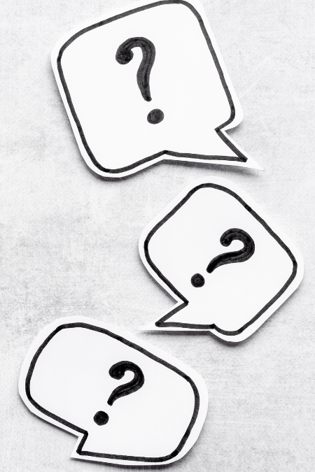Three talk bubbles with a question mark in each one. They are cut out of paper and on a marble-like table.