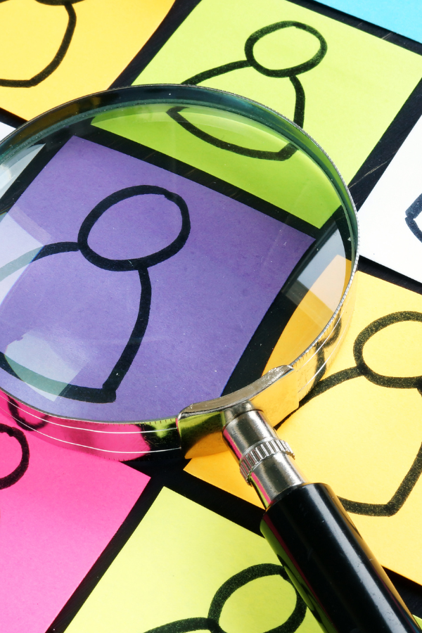 Graphics representing people drawn on different colored post it notes. A magnifying glass is focused on a purple one.