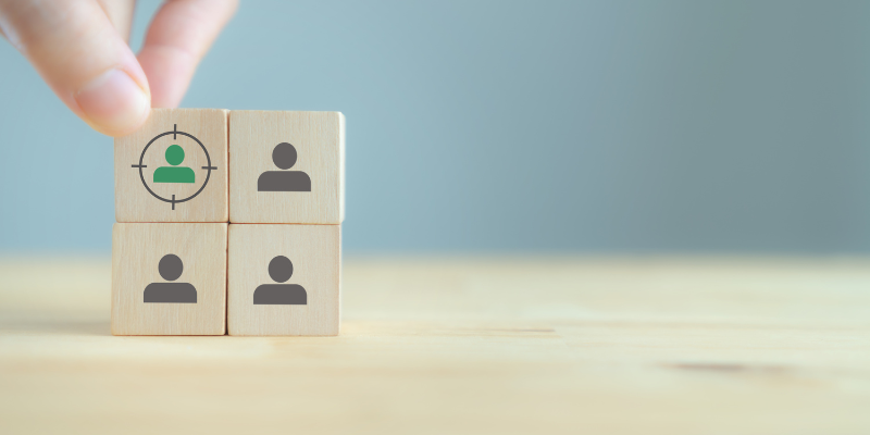 A person stacking wooden blocks with three icons of people on the blocks. The fourth has a person icon and then a target on it.