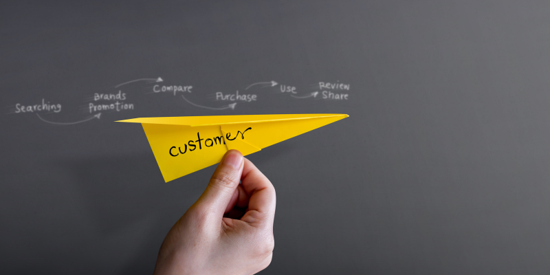 A person holding a yellow paper airplane with the word customer on it. Behind it are the steps of the customer journey.