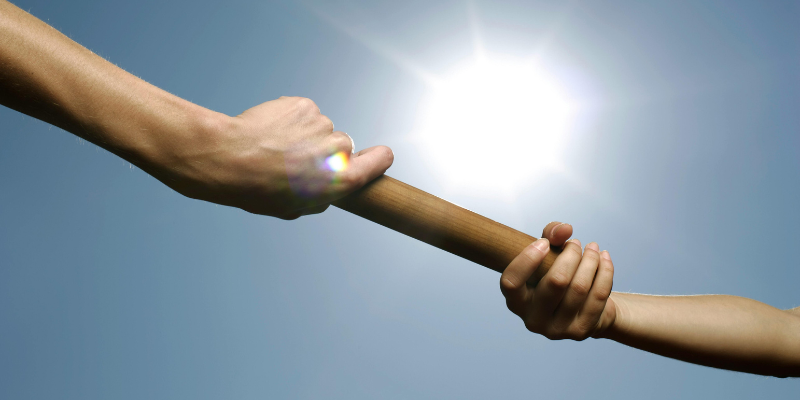 A person handing off a wooden batan off to another person